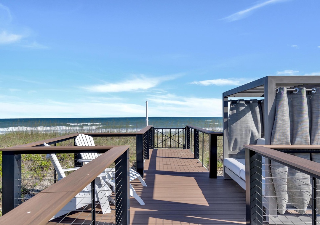 A private deck leads directly to the sandy shoreline, where white Adirondack chairs await and a shaded cabana offers a cool retreat after hours in the sun.