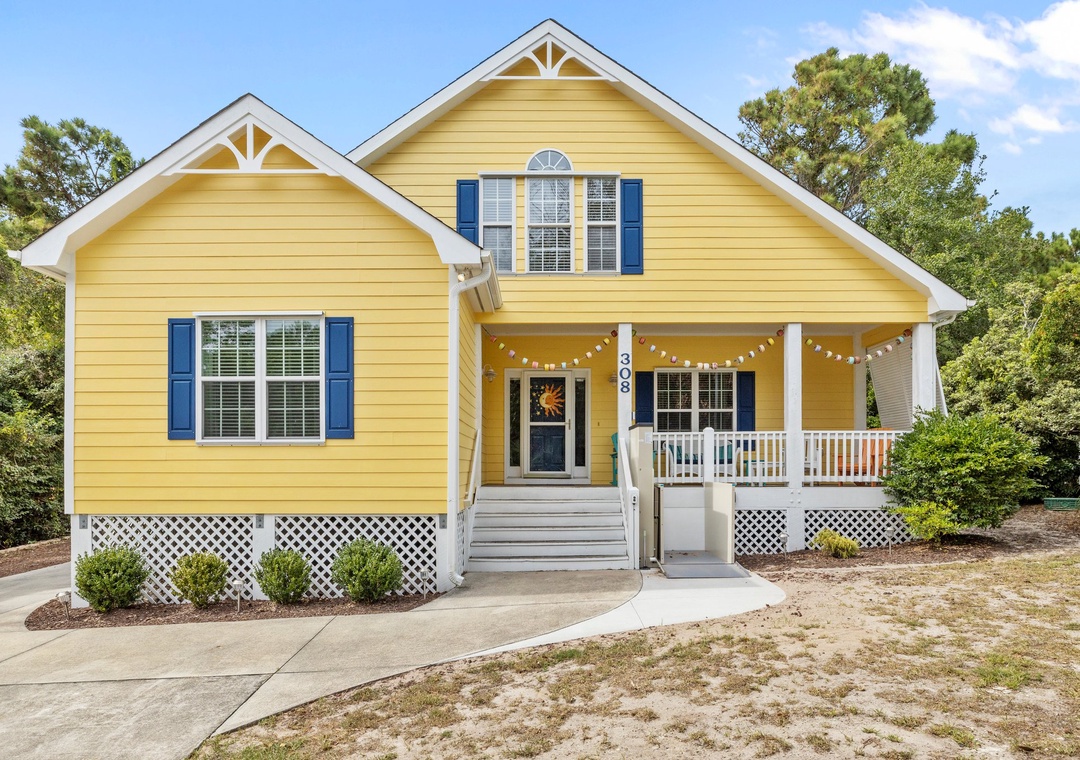 Cheerful yellow cottage with blue shutters and welcoming front porch featuring string lights and white railings.