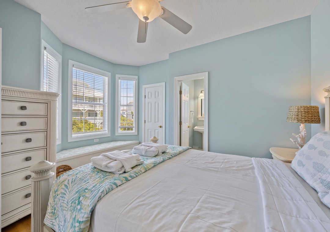 Drift off in this serene bedroom with soft blue walls, crisp linens, and a gentle ceiling fan creating the perfect coastal retreat atmosphere.