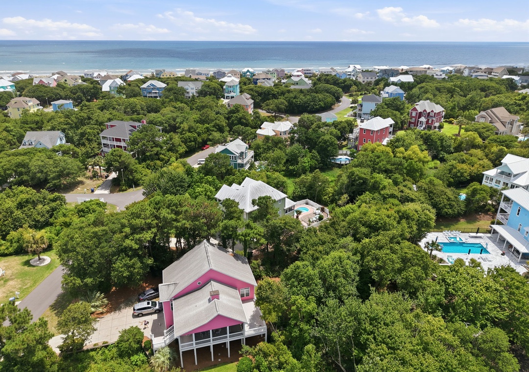 Aerial view showcasing the coastal community with beach access, vacation homes nestled among lush greenery, and the ocean visible in the distance.