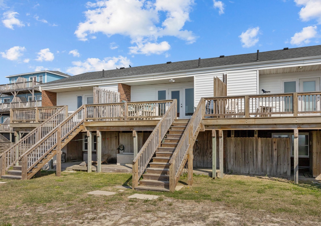 Coastal vacation rental properties featuring elevated decks and wooden staircases under a bright blue sky.