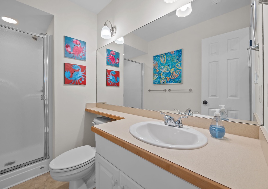 Refresh in your bright bathroom featuring a glass shower, spacious vanity, and cheerful tropical artwork that brightens your morning routine.