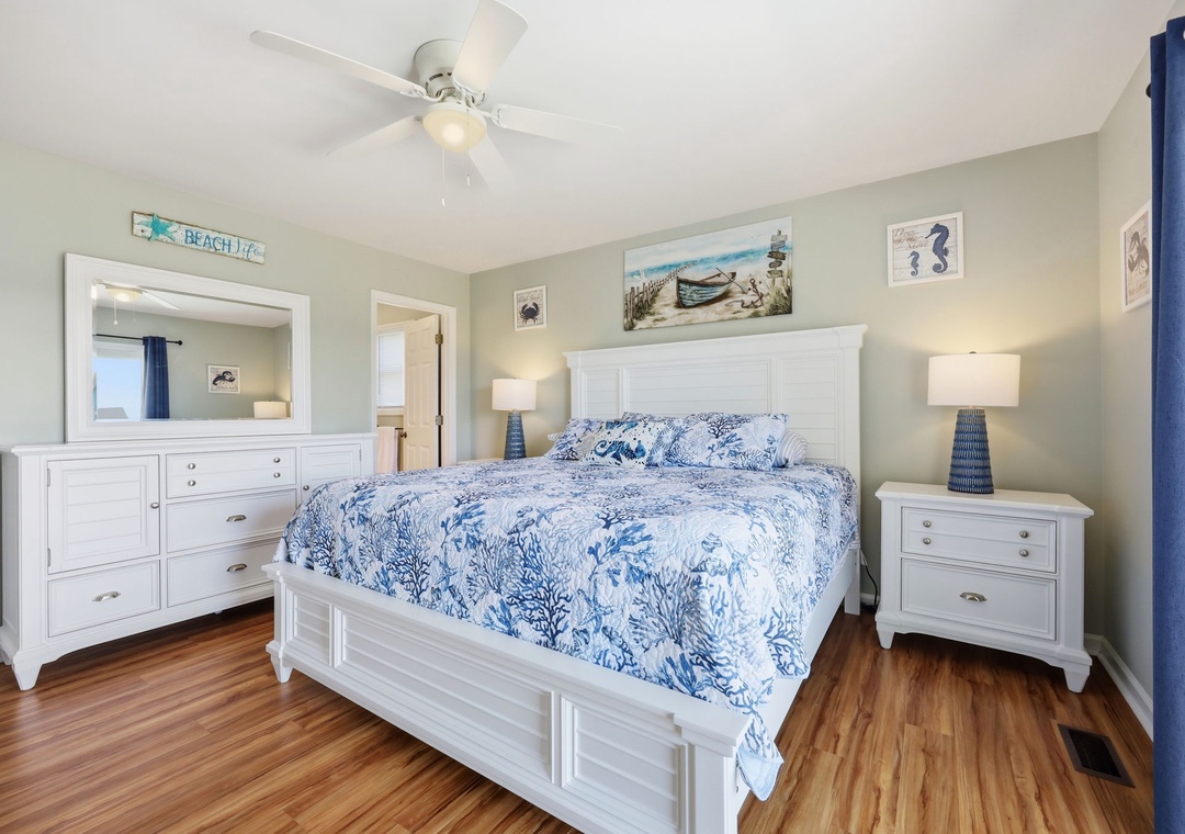 Drift off in this coastal-inspired bedroom where ocean blue bedding and crisp white furnishings create your serene seaside escape beneath the gentle breeze of a ceiling fan.