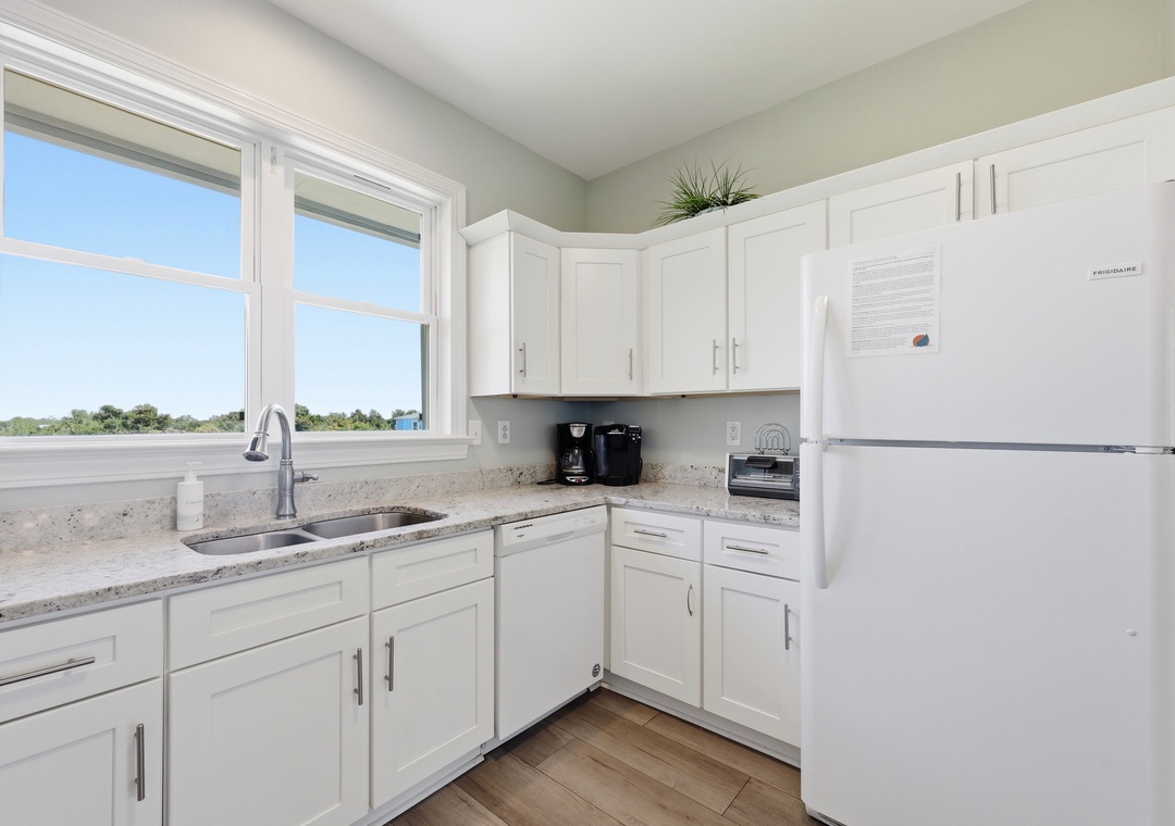 Your bright, fully-equipped kitchen invites you to brew morning coffee while natural light pours through large windows overlooking peaceful treetops. White cabinetry and granite counters create a fresh, inviting space.