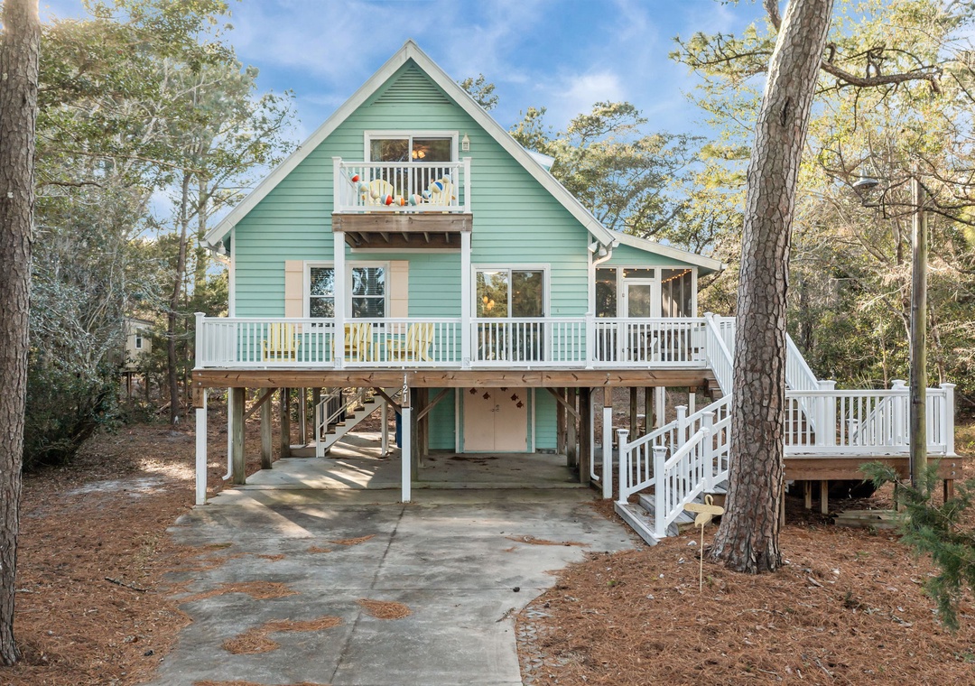 Charming coastal cottage with wraparound deck and convenient parking beneath, nestled among mature trees.