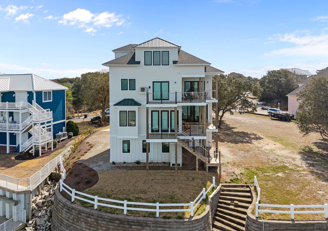 Modern four-story beach house with elevated design surrounded by coastal community and mature oak trees.