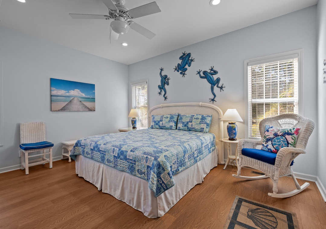 Relax in your charming bedroom with ocean-themed touches, featuring a cozy bed, wicker rocking chair, and peaceful coastal artwork.