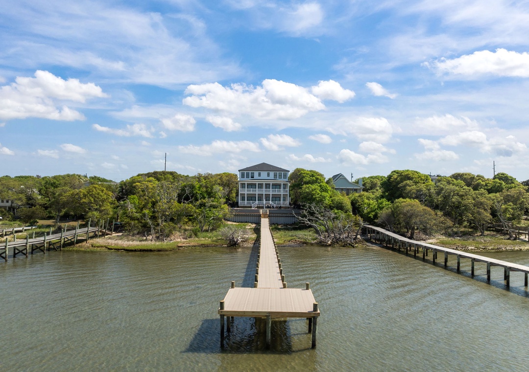 Waterfront property featuring a private dock extending into calm waters, surrounded by lush trees and coastal charm.