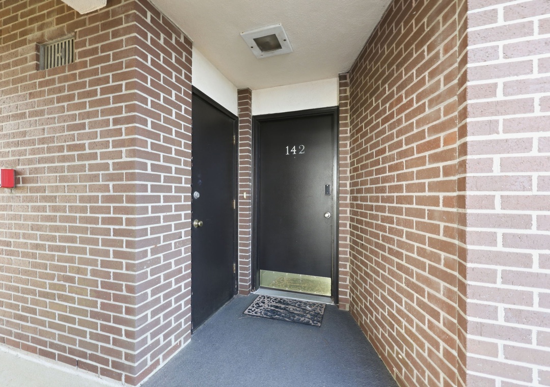 The private entrance to unit 142, framed by warm brick walls and a decorative welcome mat, marks the start of your stay.