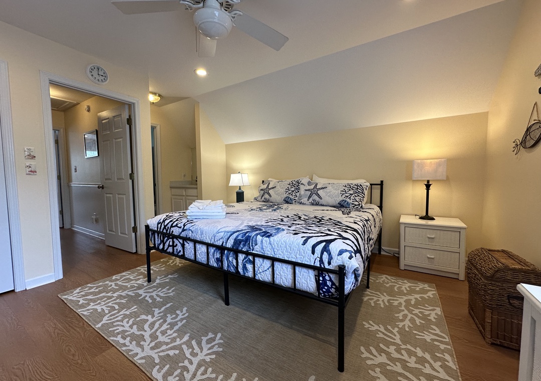 Sink into your plush coastal-themed bed after a long day, where soft linens and a gentle ceiling fan promise restful nights. Your bedside lamps cast a warm glow over polished floors and elegant décor.