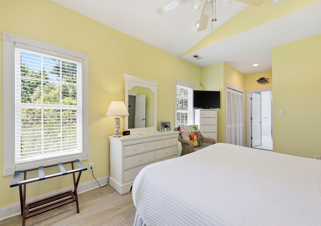 Unwind in your sunny bedroom with vaulted ceilings, a ceiling fan, and bright natural light streaming through plantation shutters. Relax in the inviting coastal decor with modern amenities.