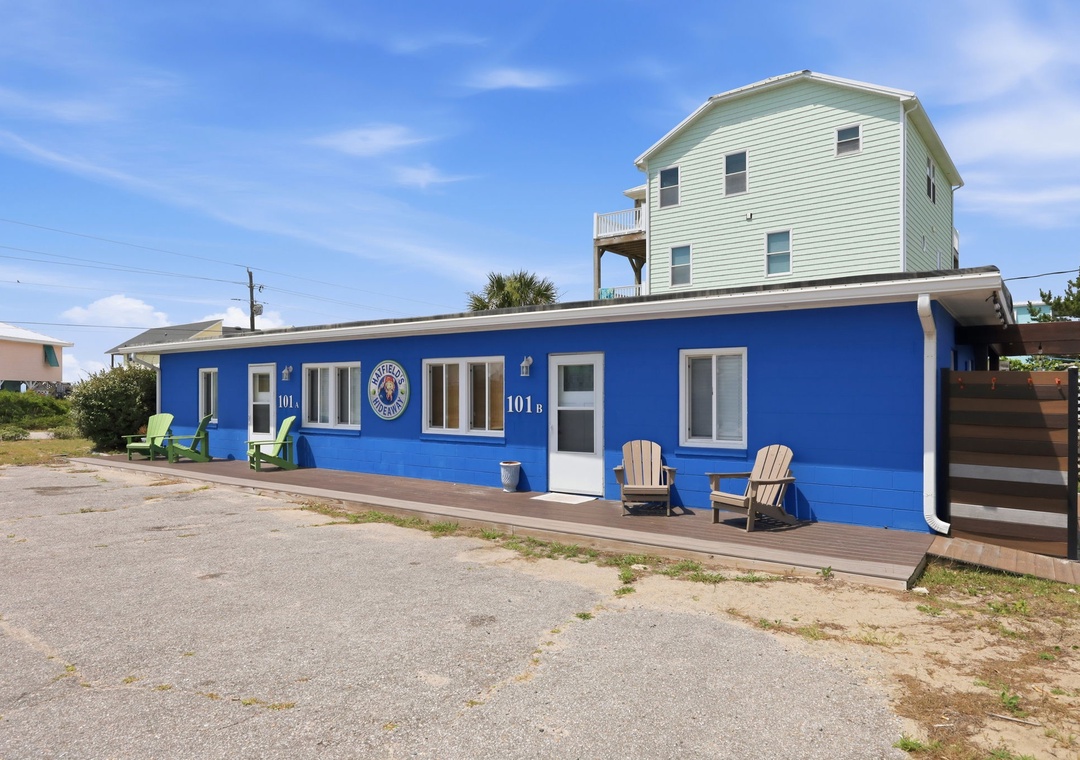 A vibrant blue beachside building with cozy Adirondack chairs on the wooden deck, offering easy access to the sand and surf.