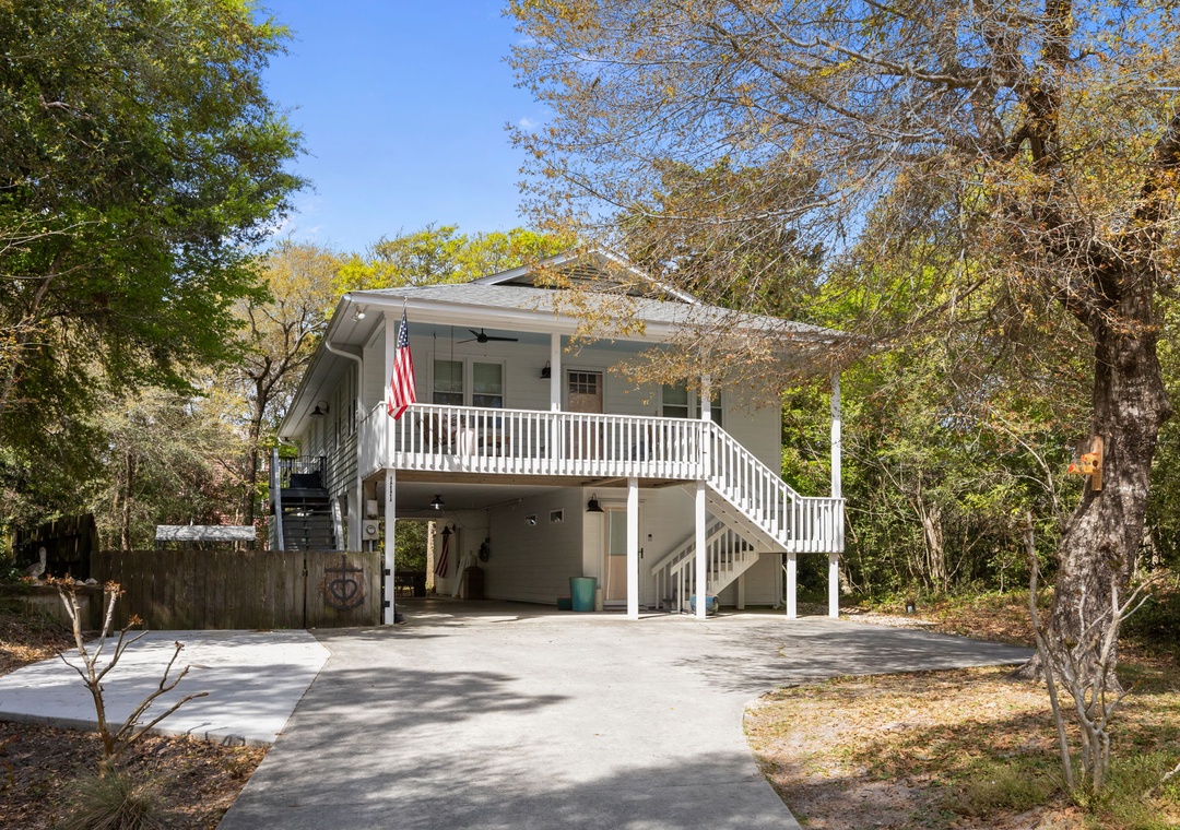 Charming elevated beach house with covered parking and spacious deck surrounded by mature trees.