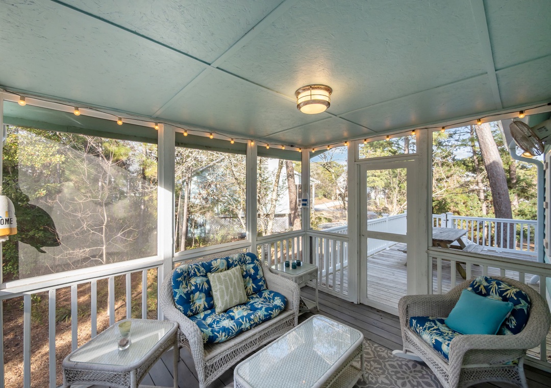 Relax in your screened-in porch with comfy wicker seating and string lights, overlooking peaceful wooded surroundings.