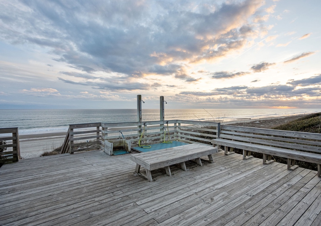 Wooden deck with seating overlooking ocean beach at sunset, perfect for evening relaxation.