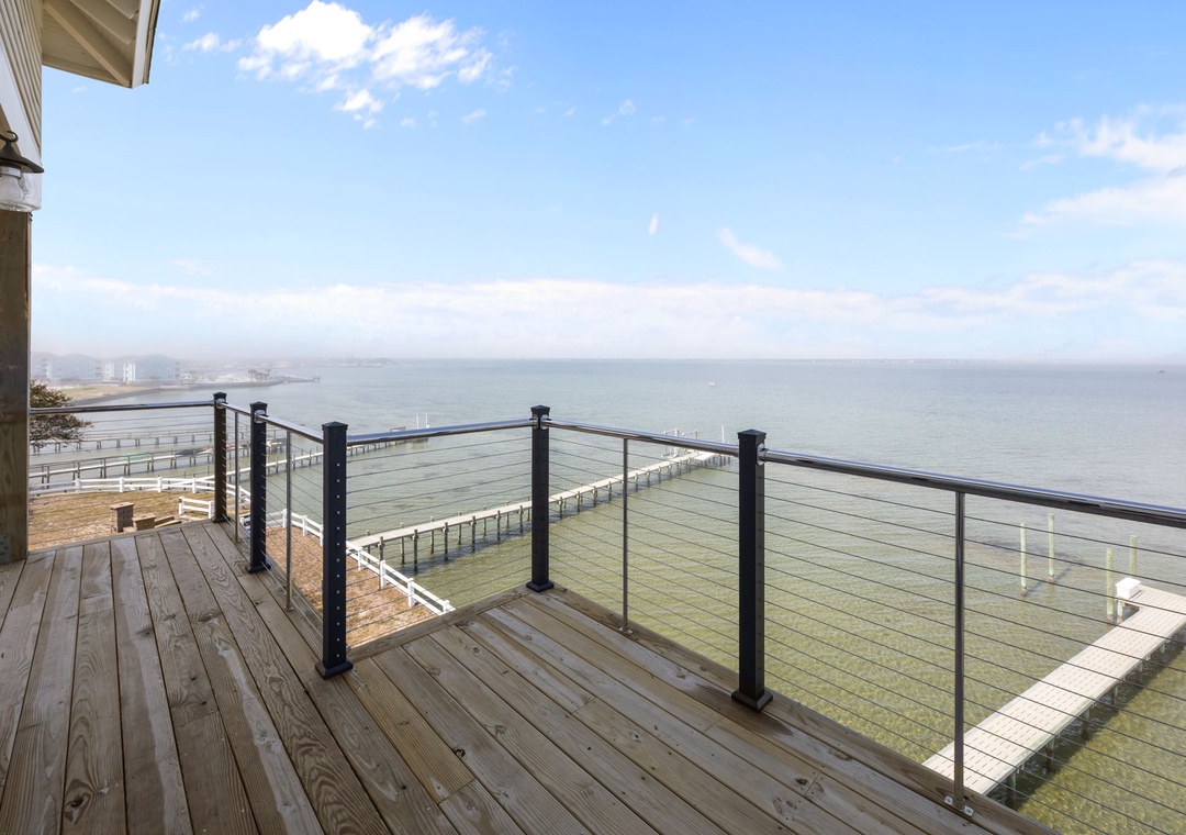 A stunning waterfront deck with panoramic ocean views and modern glass railings overlooking the peaceful coastline.