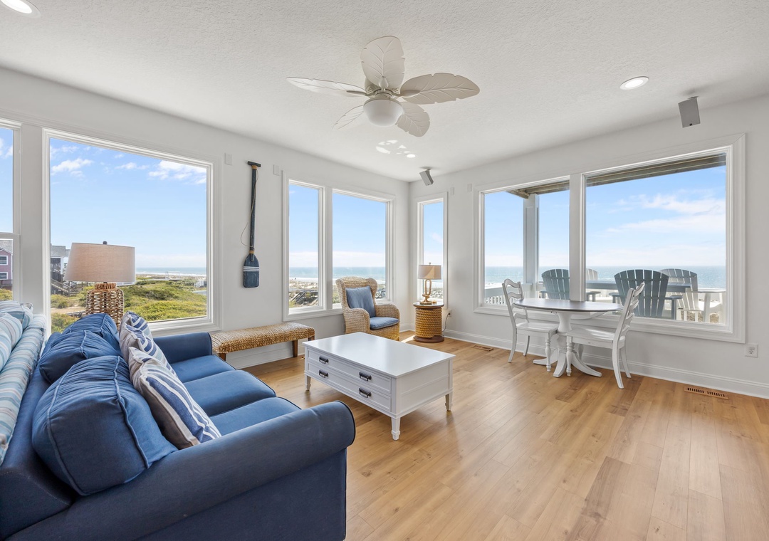 Unwind in your light-filled living space with panoramic ocean views through floor-to-ceiling windows and coastal breezes from the ceiling fan.