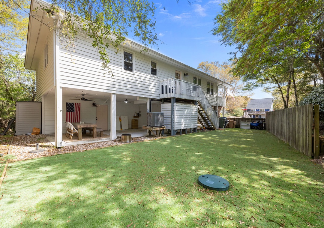 Two-story white property with covered outdoor area and spacious fenced backyard surrounded by mature trees.