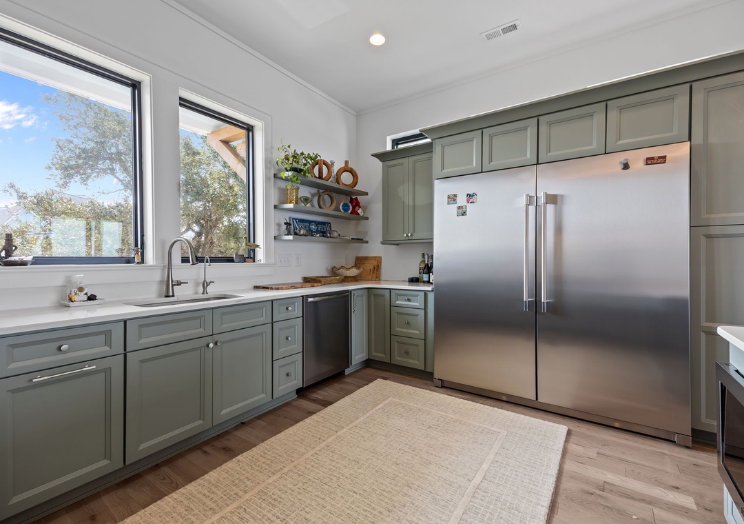 Cook with ease in your fully-equipped kitchen featuring sage-green cabinetry, stainless steel appliances, and garden views that inspire culinary creativity.