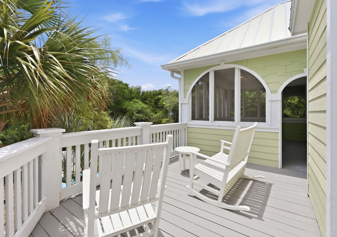 The property features a peaceful deck surrounded by lush tropical landscaping and clear blue skies, providing a serene arrival experience.