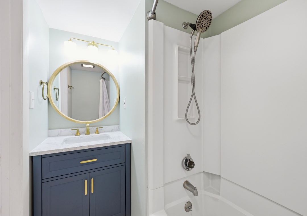 Your freshly updated bathroom features elegant gold accents, a sleek navy vanity with marble countertop, and a bright tub-shower combination ready for your comfort.