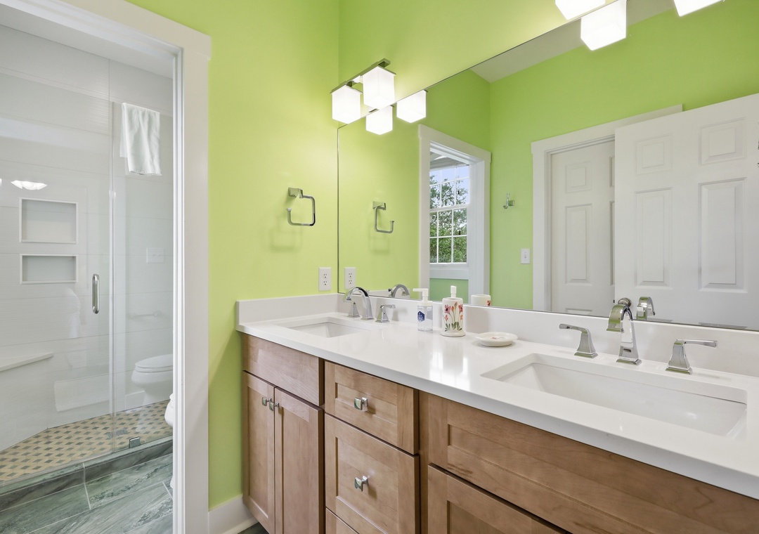 Your private bathroom features cheerful green walls, dual sinks with elegant fixtures, and a spacious walk-in shower with fresh white tile—perfect for refreshing mornings.