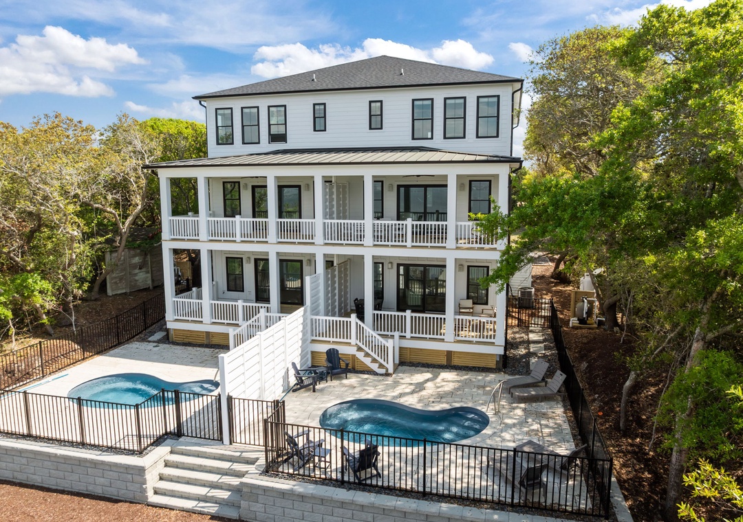Modern three-story vacation home with wraparound porches, private pool, and hot tub nestled among lush trees.