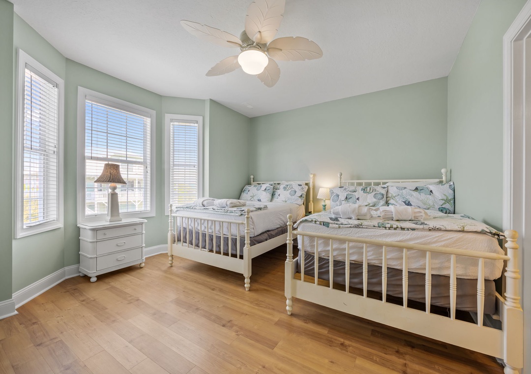 Unwind in your serene retreat featuring twin beds with botanical linens, calming sage walls, and a gentle ceiling fan.