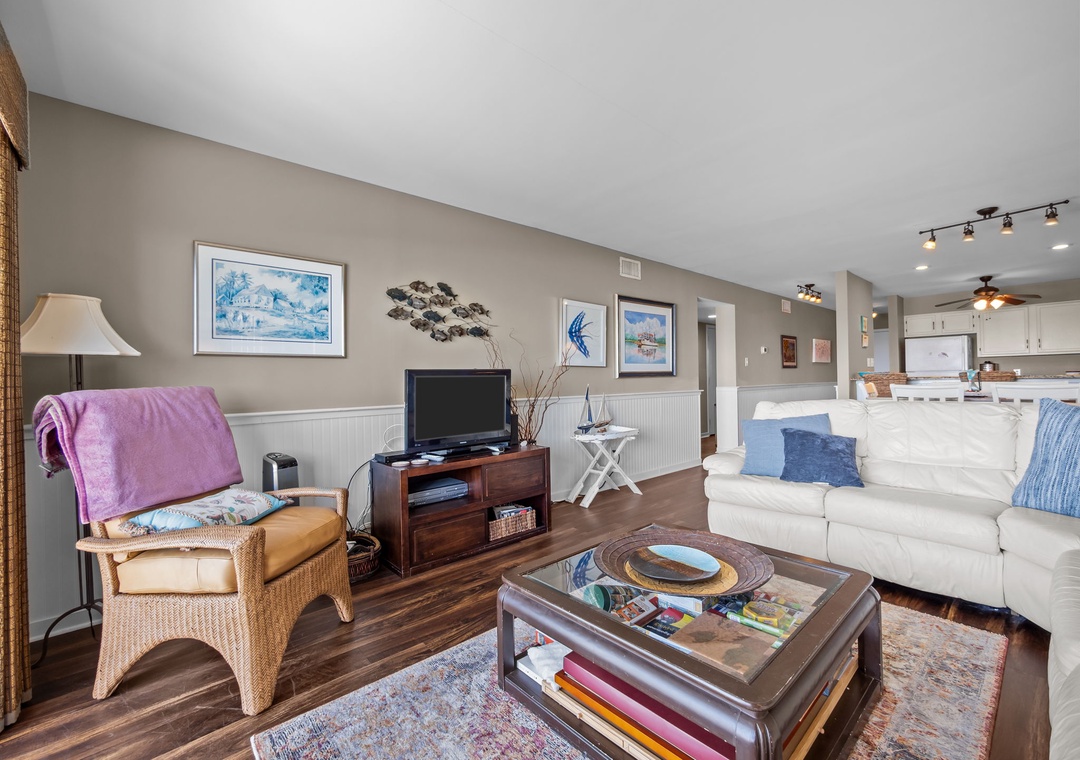 Relax in your spacious living room with coastal art, comfortable seating, and an open kitchen perfect for beach vacation evenings.