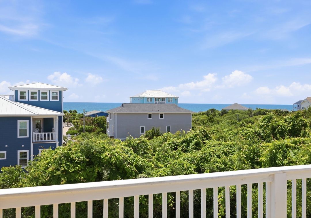 Coastal homes nestle amid lush greenery, with the sparkling ocean visible beyond the dunes, marking your arrival to this beach community.