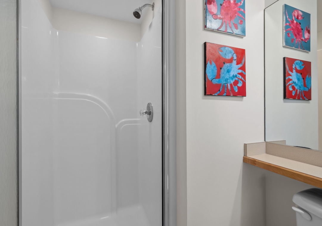 Step into your bright bathroom featuring a pristine glass shower with modern fixtures and cheerful coastal artwork to brighten your morning routine.