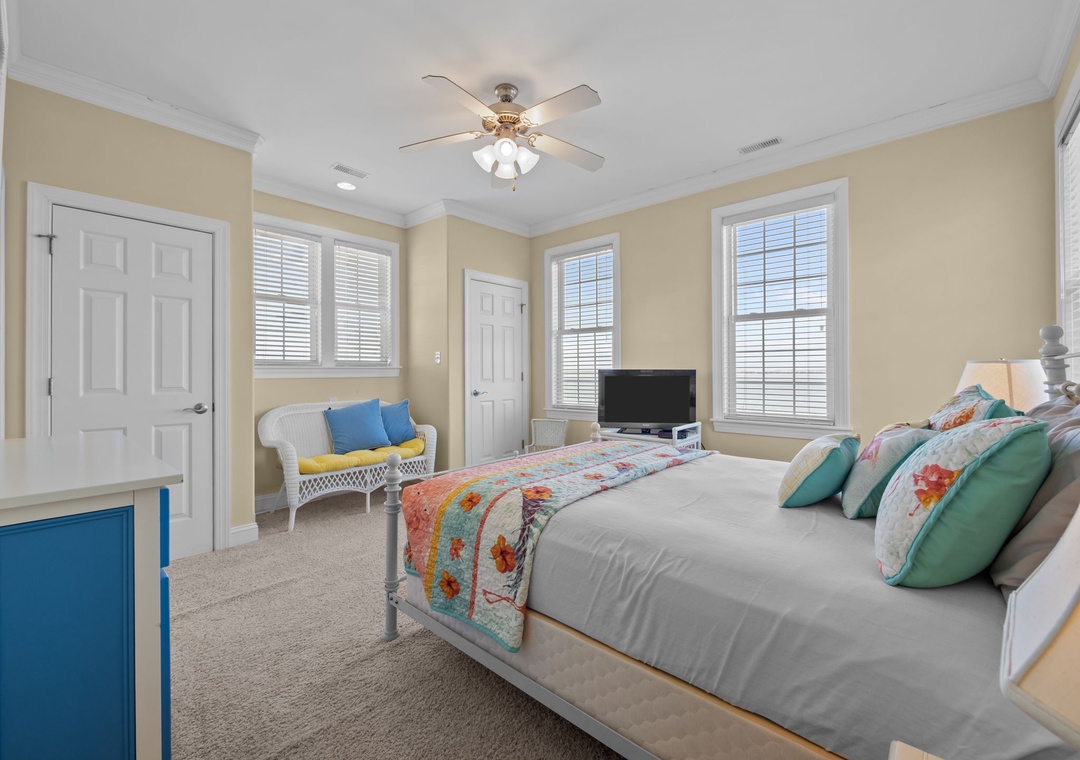 Unwind in your bright, cheerful bedroom with colorful quilted bedding, cozy seating nook, and natural light streaming through multiple windows.