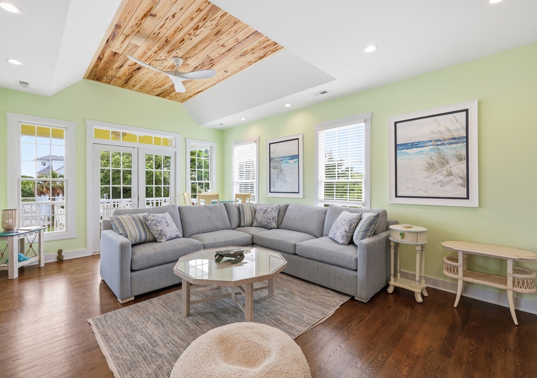 Unwind in your bright, coastal living room with vaulted wood ceilings, plush seating, and serene beach views framed by sunlit windows—your peaceful retreat awaits.