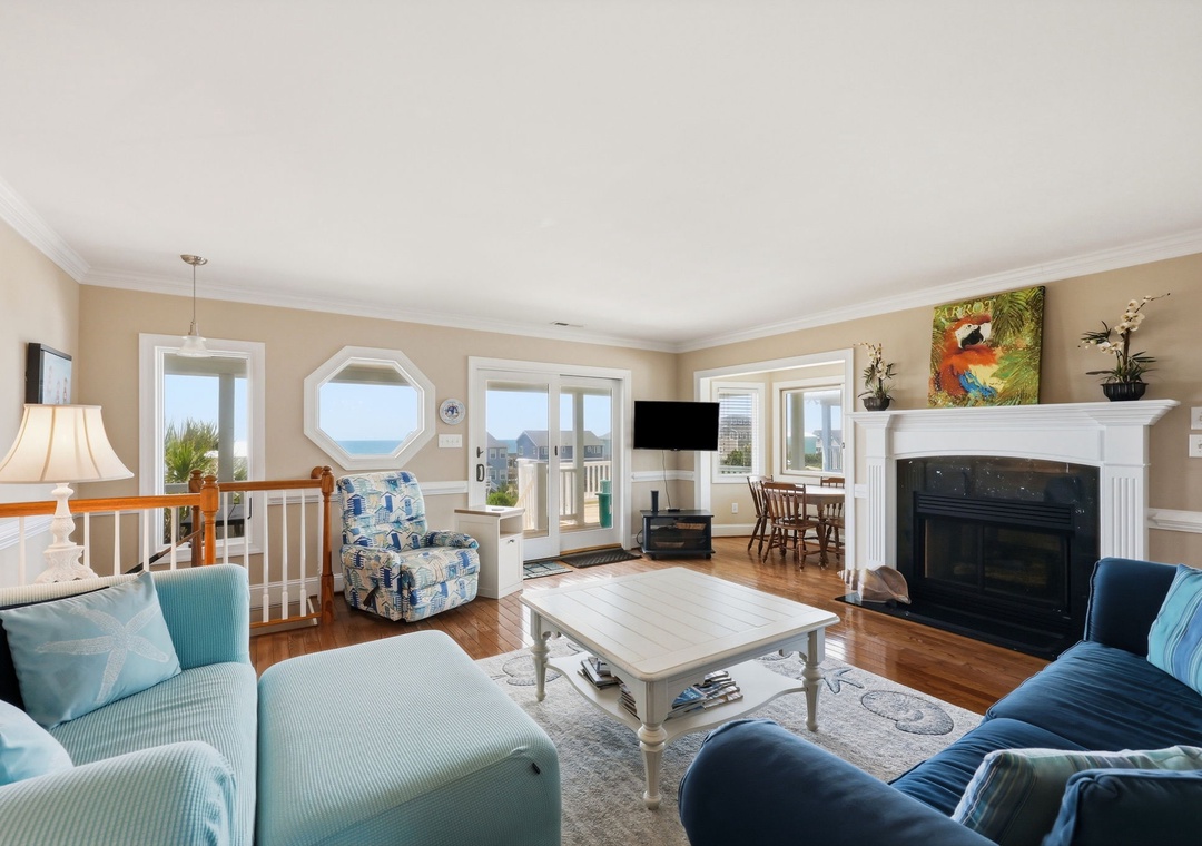 Relax in your bright, coastal living room with a crackling fireplace, sweeping ocean views through multiple windows, and plush seating perfect for unwinding after a day at the beach.
