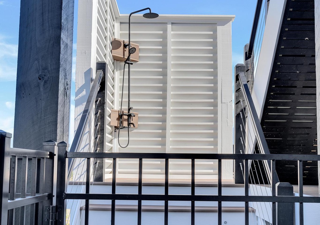 Private outdoor shower with slatted privacy screen and warm wood decking, set against clear blue skies for a refreshing open-air experience.