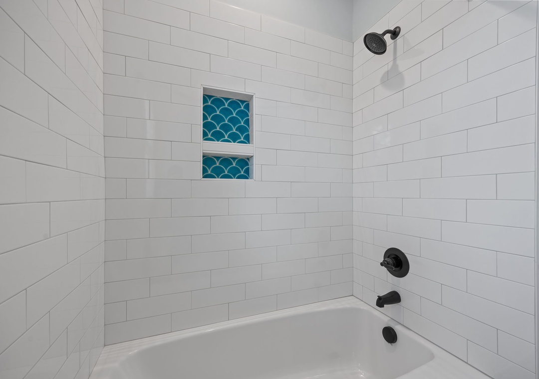 Unwind in your pristine spa-like bathroom featuring clean subway tiles, a spacious tub, and charming turquoise accent niches for a refreshing retreat.