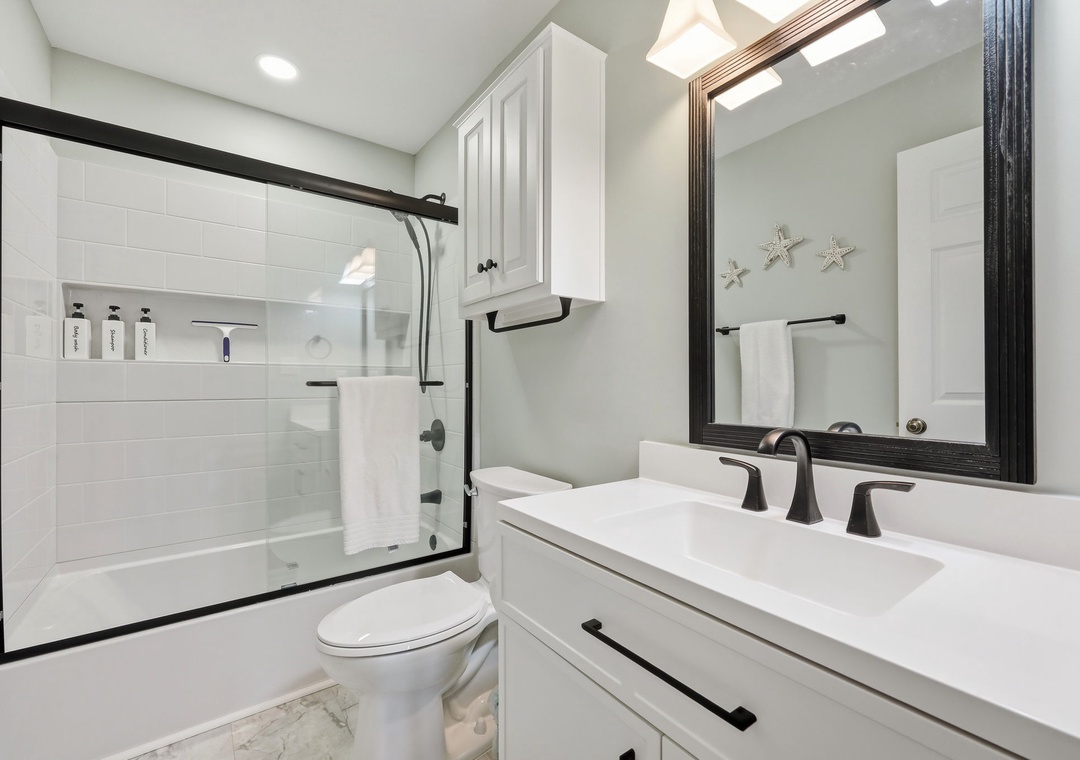 Refresh in your pristine bathroom featuring a sleek walk-in shower, coastal starfish accents, and modern fixtures—your personal spa awaits after beach adventures.