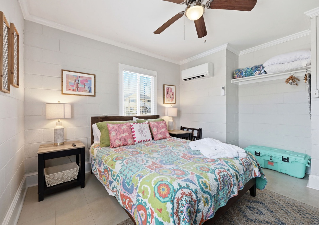 Unwind in your coastal retreat with a plush bed dressed in vibrant linens, ceiling fan to keep you cool, and a cozy reading nook by the window where you can relax after a day of exploring.