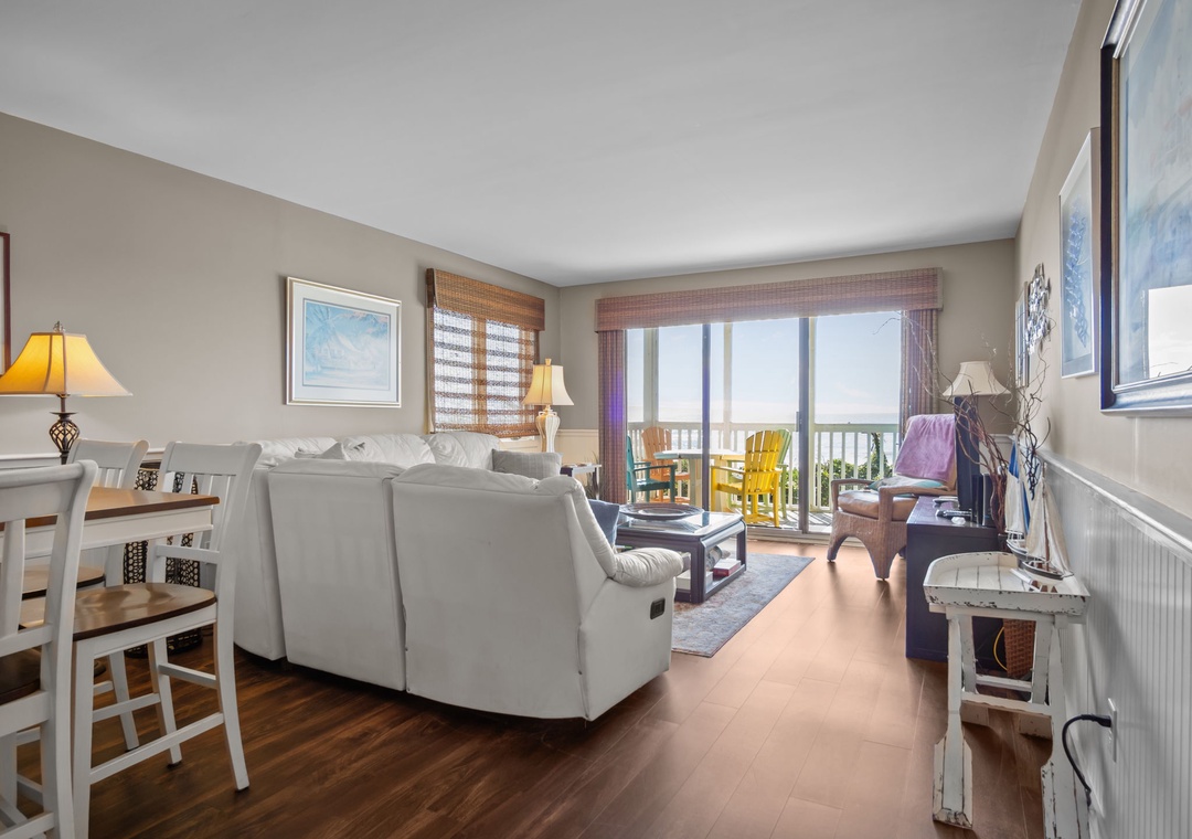 Relax in your bright living space with comfy seating, dining area, and balcony overlooking colorful outdoor furniture—perfect for morning coffee.