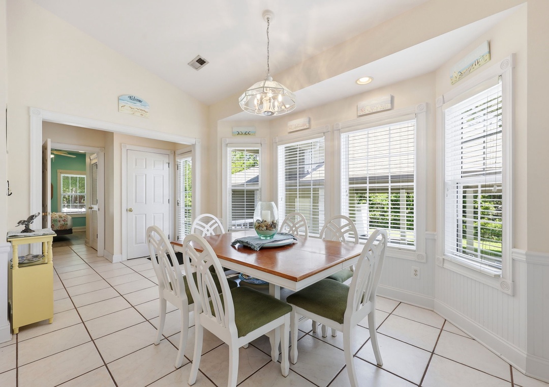 Gather around this bright dining space for meals bathed in natural light. The coastal-inspired table seats eight comfortably, with white cabinetry and tile flooring creating a fresh, airy feel.