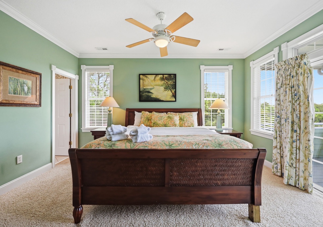Unwind in your serene retreat with soft sage walls, a plush king bed, and gentle ceiling fan breeze. Natural light fills the space while balcony doors invite fresh air and tropical views.