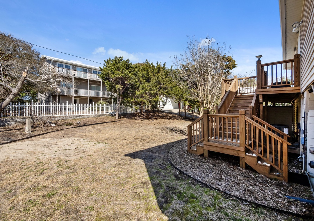 Wooden deck and stairs lead to a spacious backyard surrounded by coastal trees and neighboring properties.
