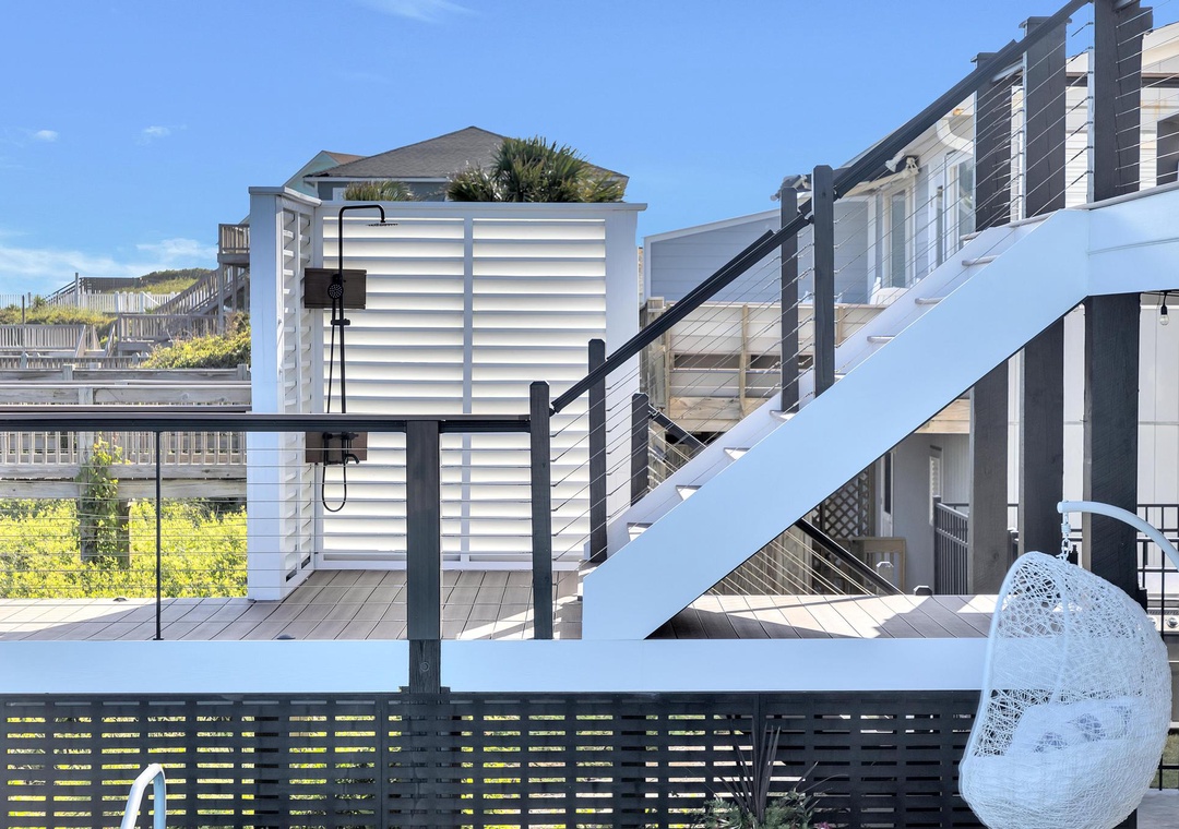 This coastal property features multiple tiered decks and staircases, offering easy access to beach activities. The modern exterior is surrounded by dunes and neighboring homes.