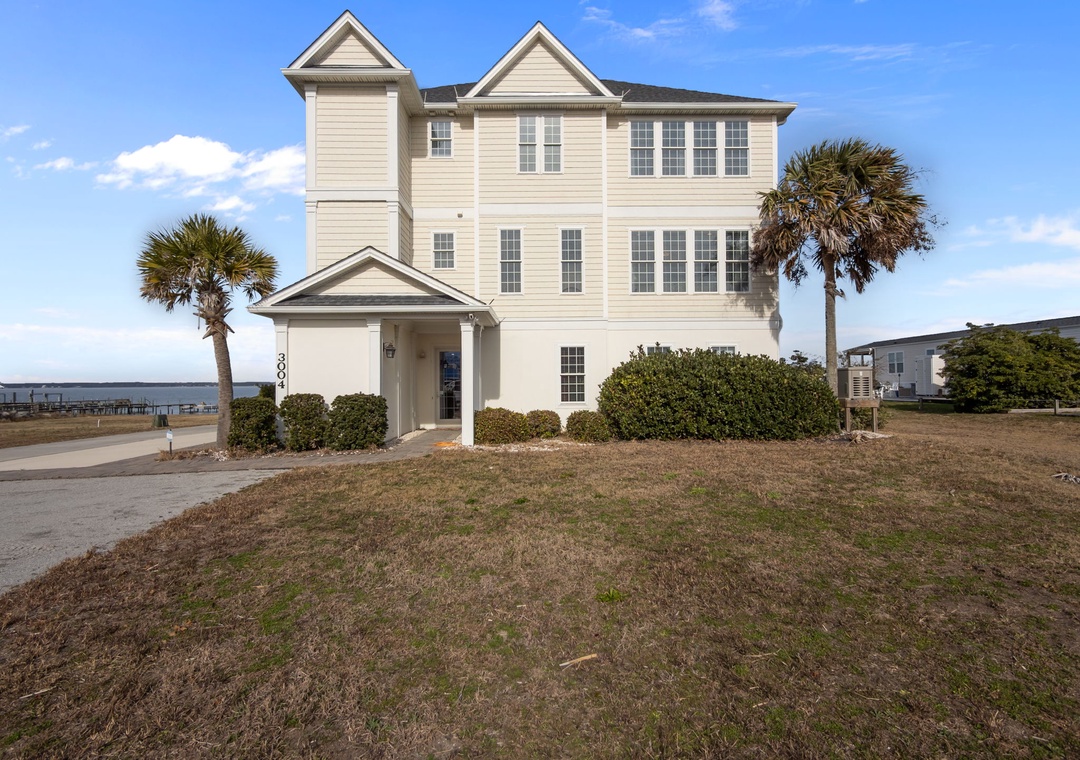 A beautiful three-story waterfront vacation home featuring classic coastal architecture with palm trees and nearby water access.