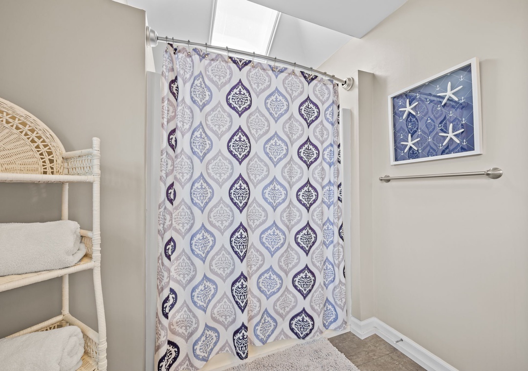 Fresh towels await you in this bright bathroom featuring a stylish patterned shower curtain and coastal-themed artwork.