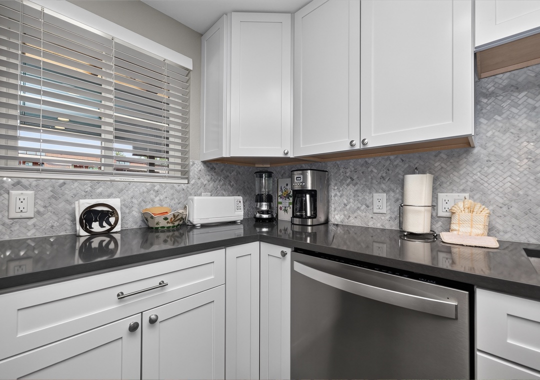 Your bright, modern kitchen features sleek white cabinets, stylish herringbone backsplash, and spacious counters for preparing meals. Coffee maker ready for your morning brew, with storage for all your travel essentials.