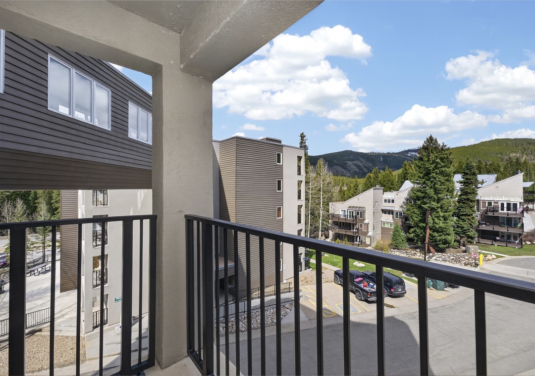 A covered balcony frames a stunning mountain view, overlooking nearby buildings and evergreen-lined peaks—your peaceful retreat amidst nature.