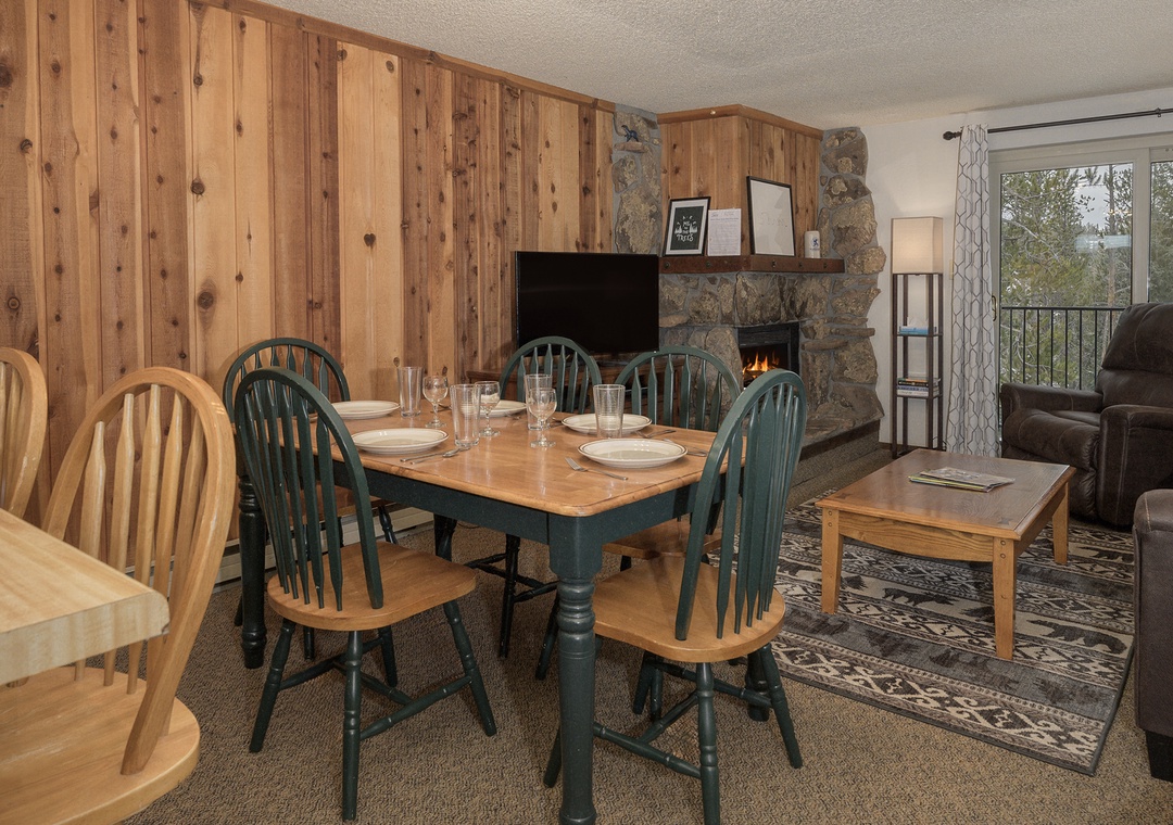 Gather around your cozy dining table with warm wood walls and crackling fireplace creating the perfect mountain retreat atmosphere.