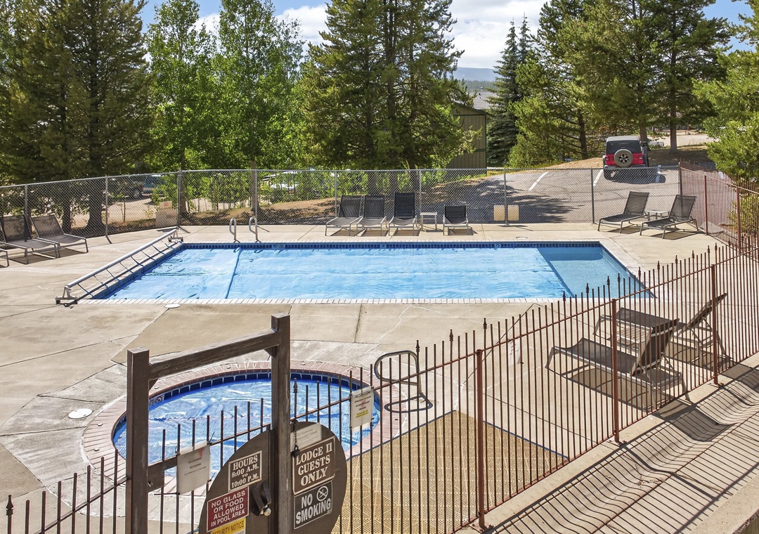 A sun-drenched pool area surrounded by mature pines and mountain scenery, with lounge chairs ready for relaxing afternoons and a hot tub for starlit soaks.