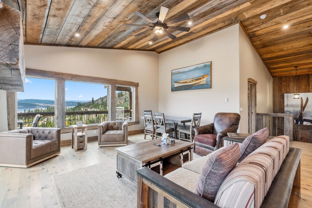 Your spacious living area at 128 GCR 4034 features rustic wood beam ceilings, comfortable seating, and stunning panoramic views through expansive windows.